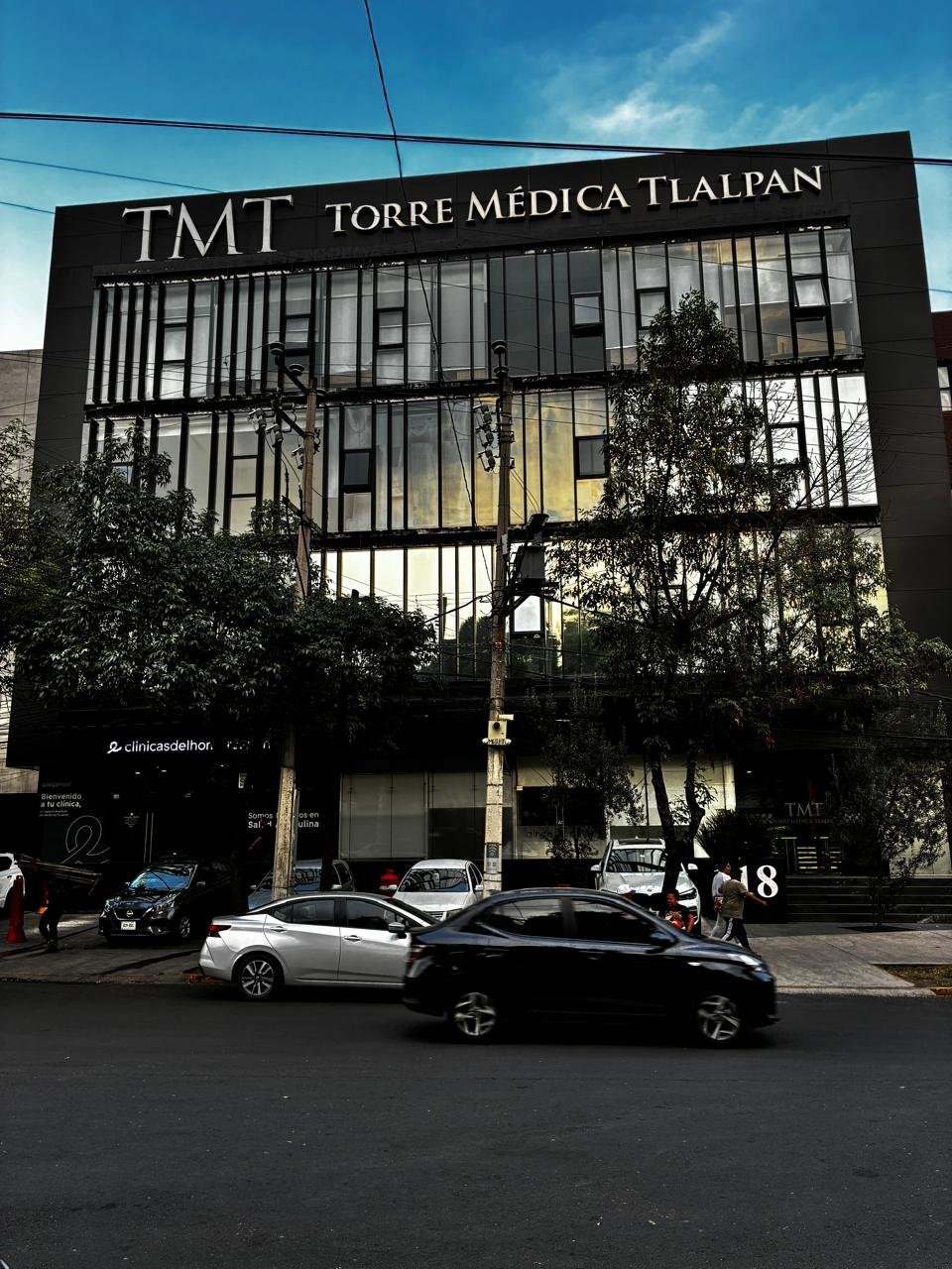 Modern black medical building TMT Torre Medica Tlalpan with large windows and cars parked in front under blue sky