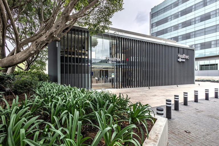 Modern black corrugated building with vertical slats, green landscaping, and bollards in urban courtyard setting